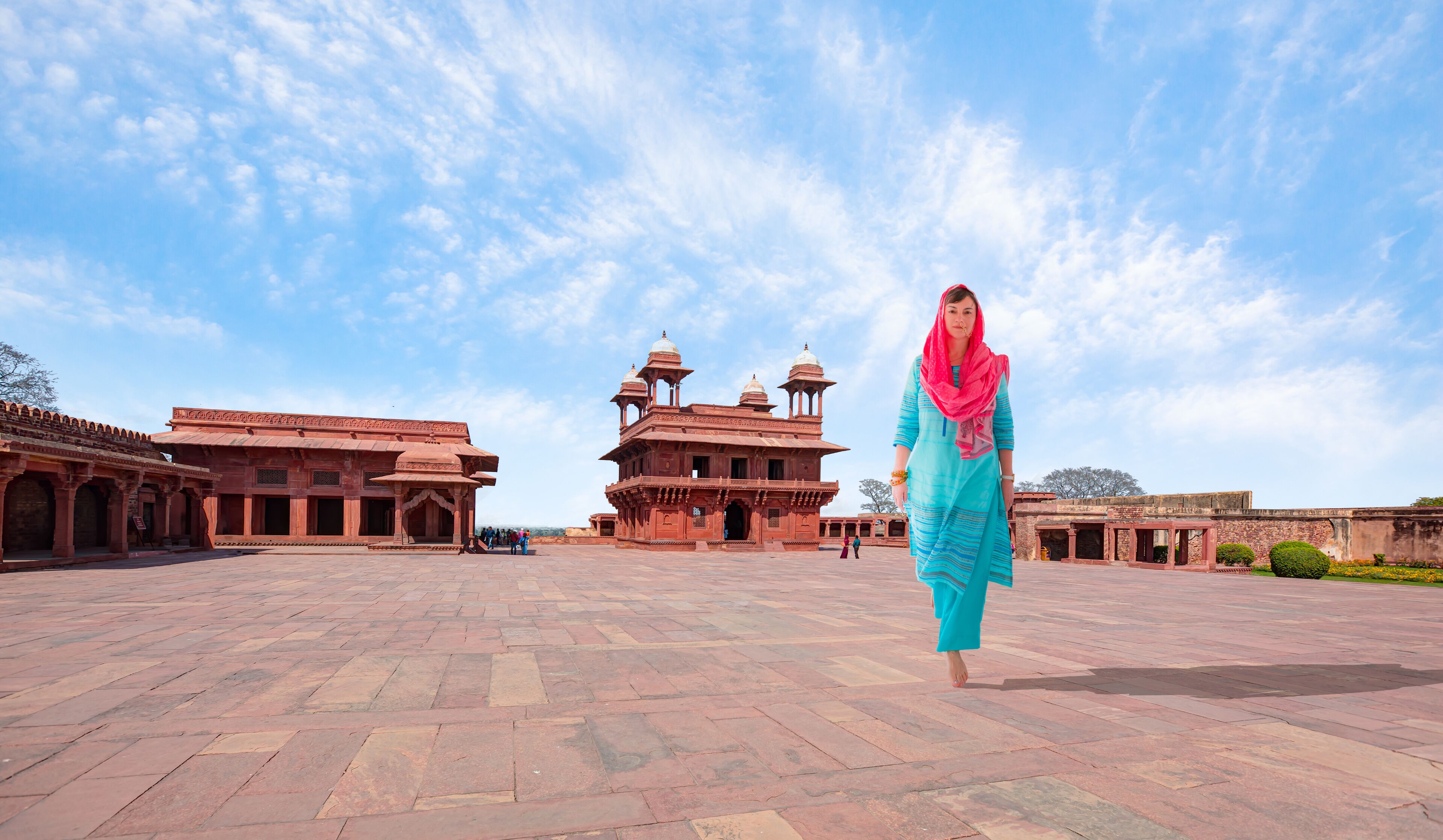A historic building with domes and arches, a paved courtyard, and a clear sky.