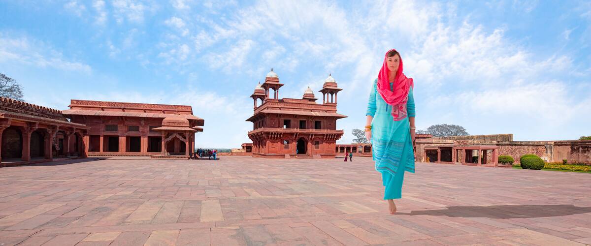 A historic building with domes and arches, a paved courtyard, and a clear sky.