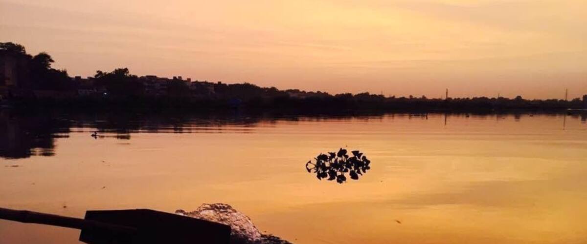 A calm river at sunset with a group of birds on the water and a boat in the foreground.