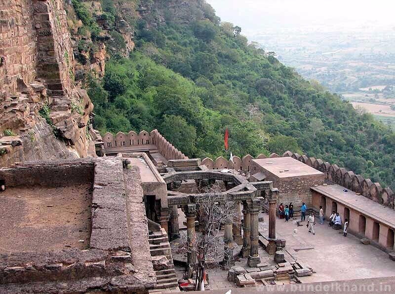 An ancient fort with stone walls and a central tower, surrounded by lush green hills.