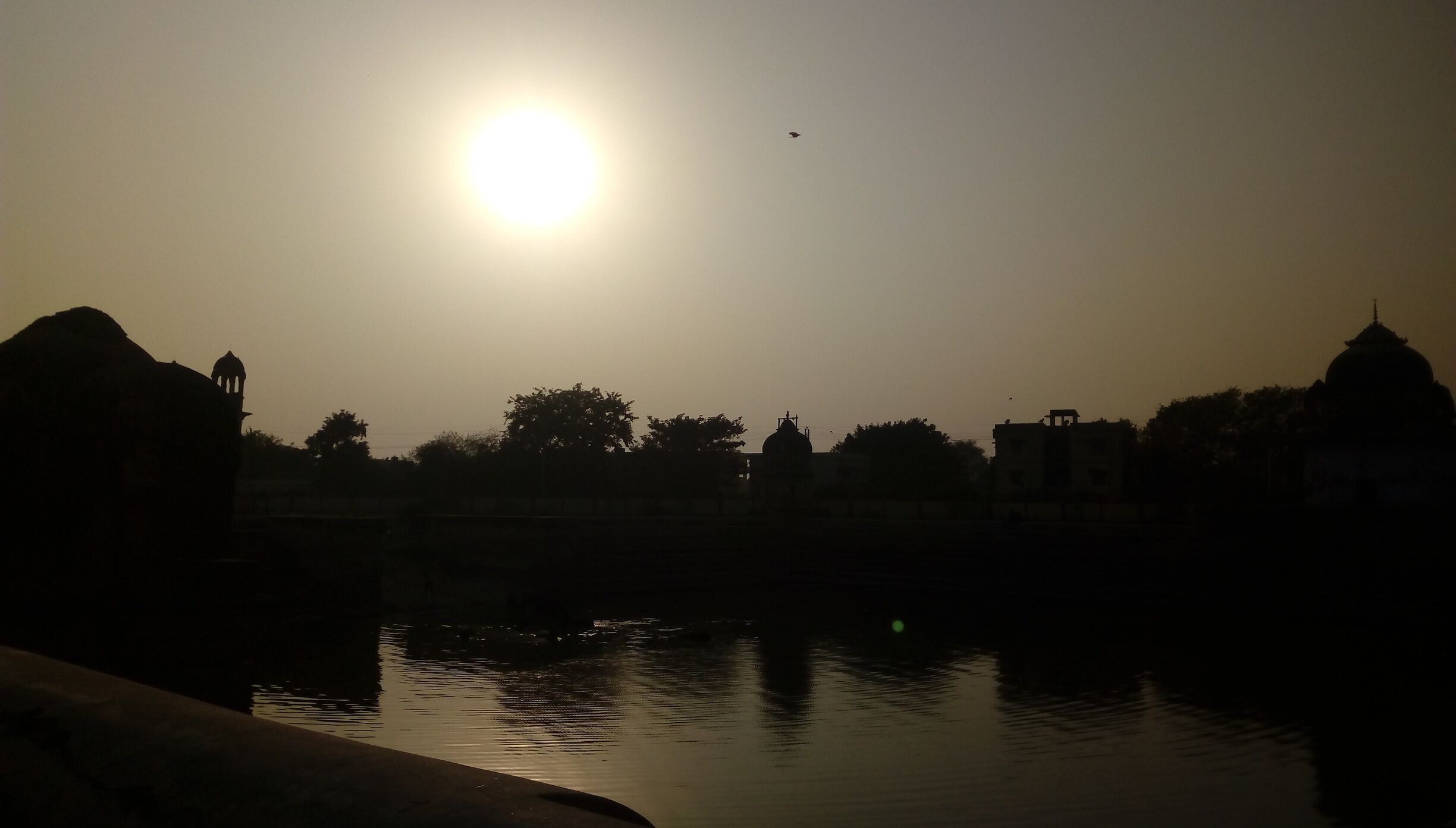 A sunset over a body of water with silhouettes of buildings and a dome structure.