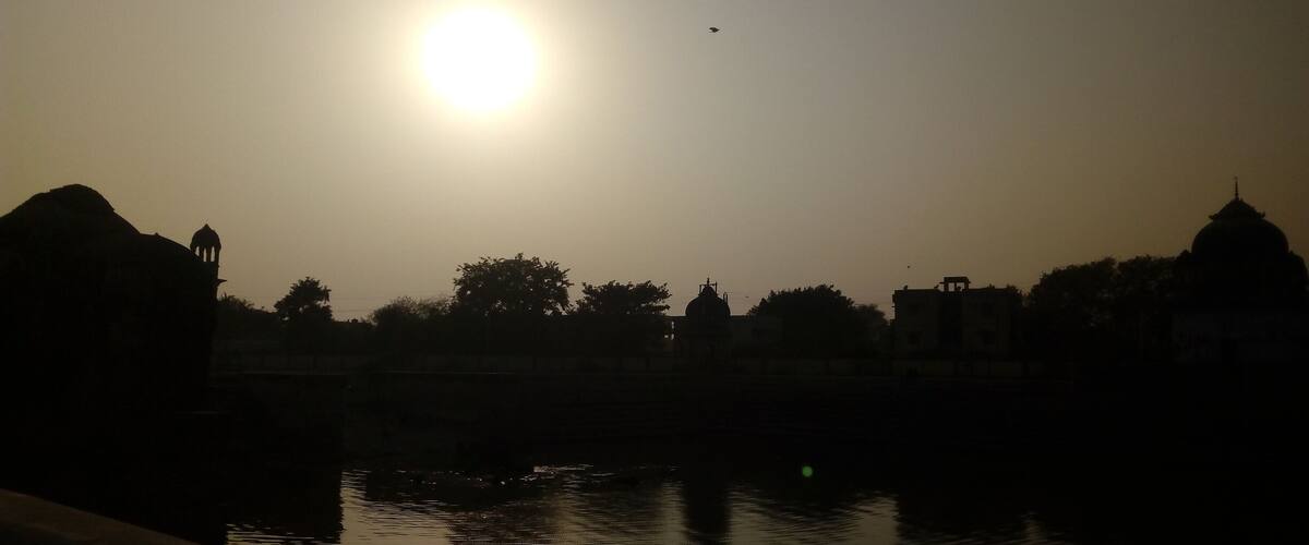 A sunset over a body of water with silhouettes of buildings and a dome structure.