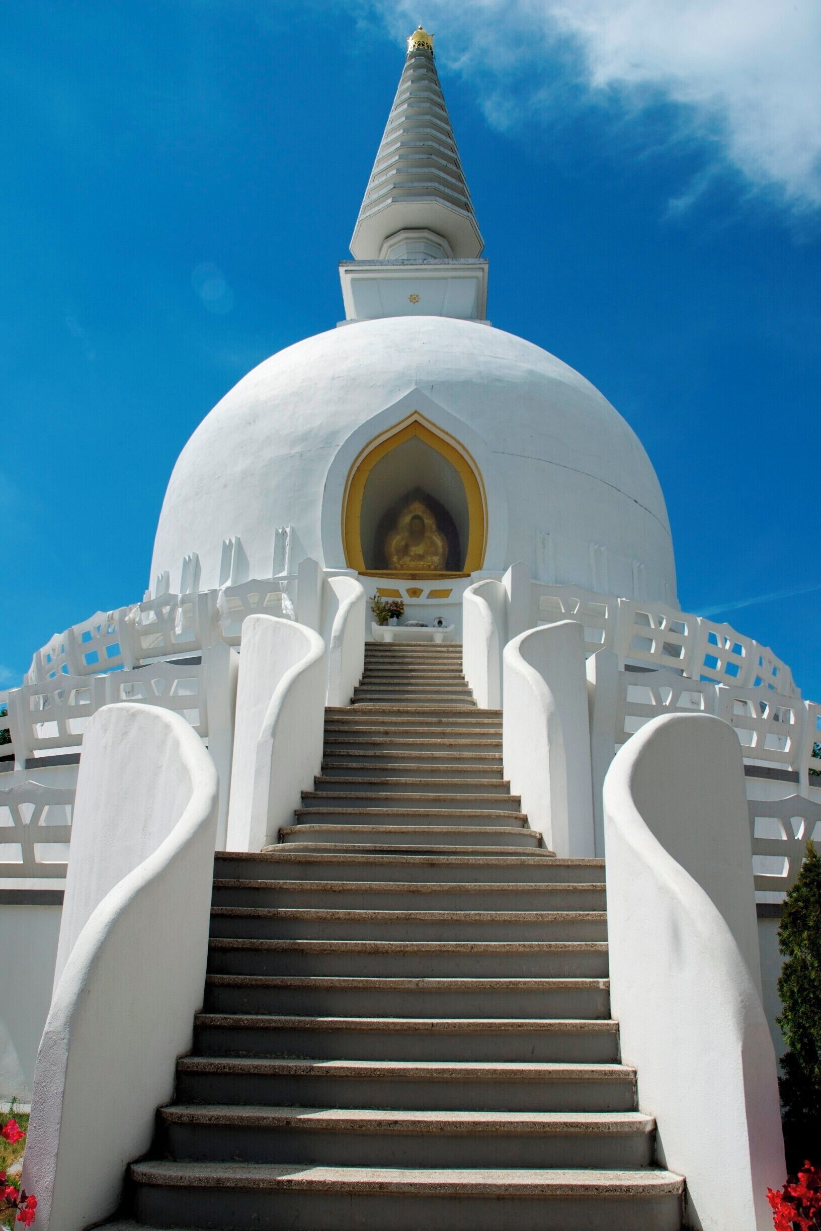 A white stupa with a golden spire, surrounded by white railings and a staircase leading up to it.
