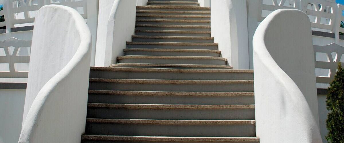 A white stupa with a golden spire, surrounded by white railings and a staircase leading up to it.