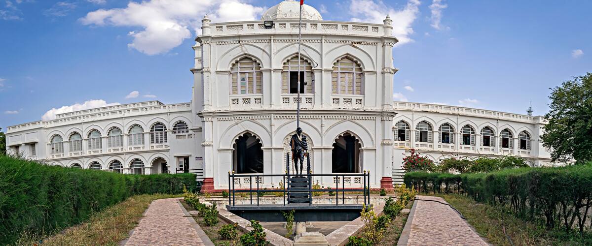 A large white building with arched windows and a central dome, surrounded by a garden and a pathway.