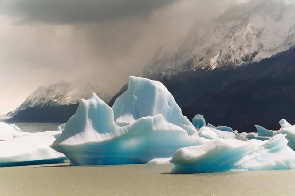 Large icebergs in a body of water with mountains in the background.