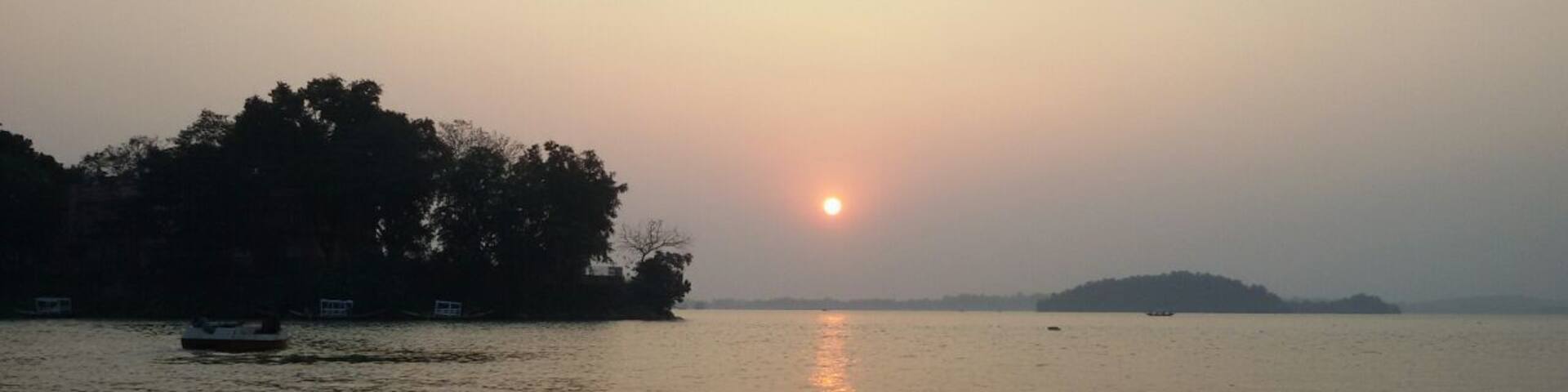 A calm lake at sunset with a boat on the left and a small island in the center.