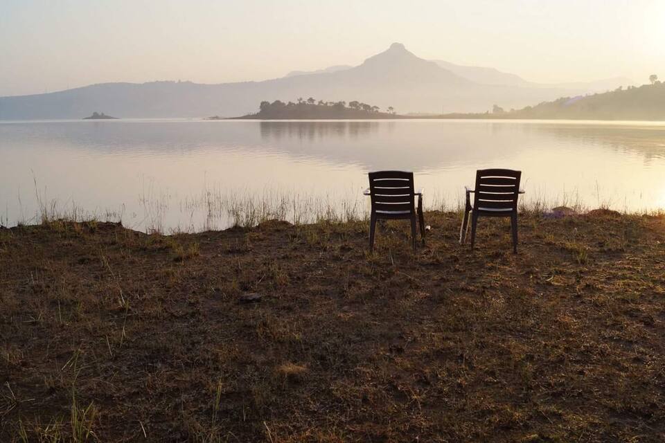 Two chairs facing a calm lake with a distant mountain and a small island.