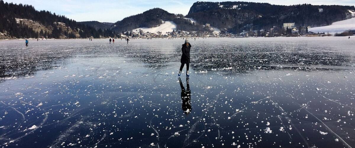 A frozen lake with people ice skating, surrounded by hills and a town in the background.