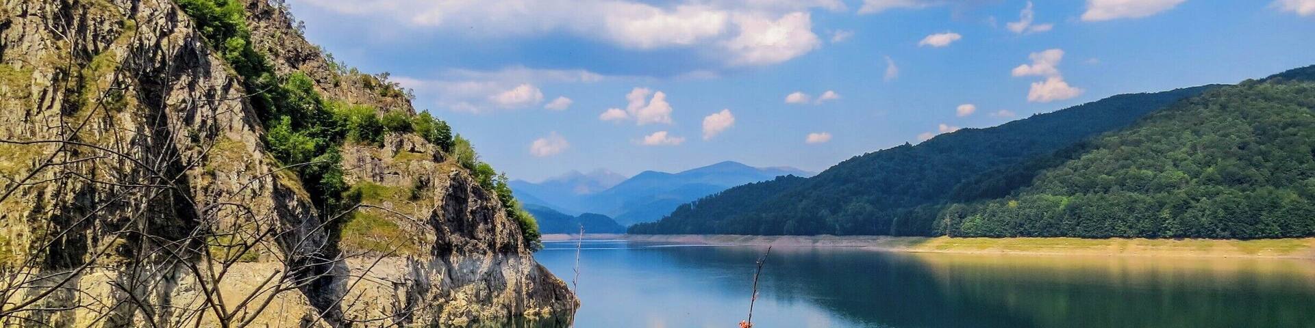 A calm lake surrounded by rocky cliffs and lush greenery.