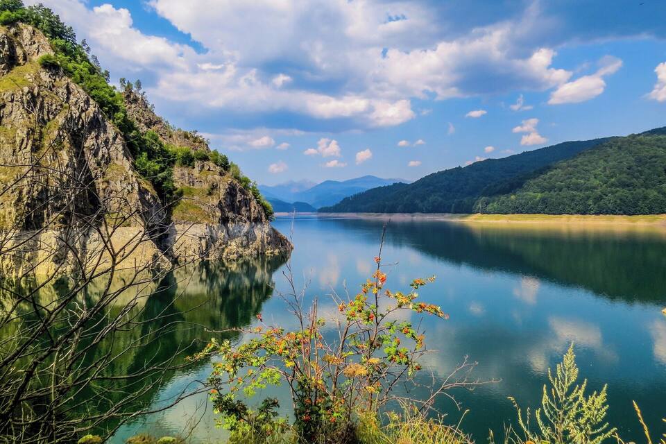 Un lac paisible, bordé de falaises rocheuses et d’une végétation luxuriante.