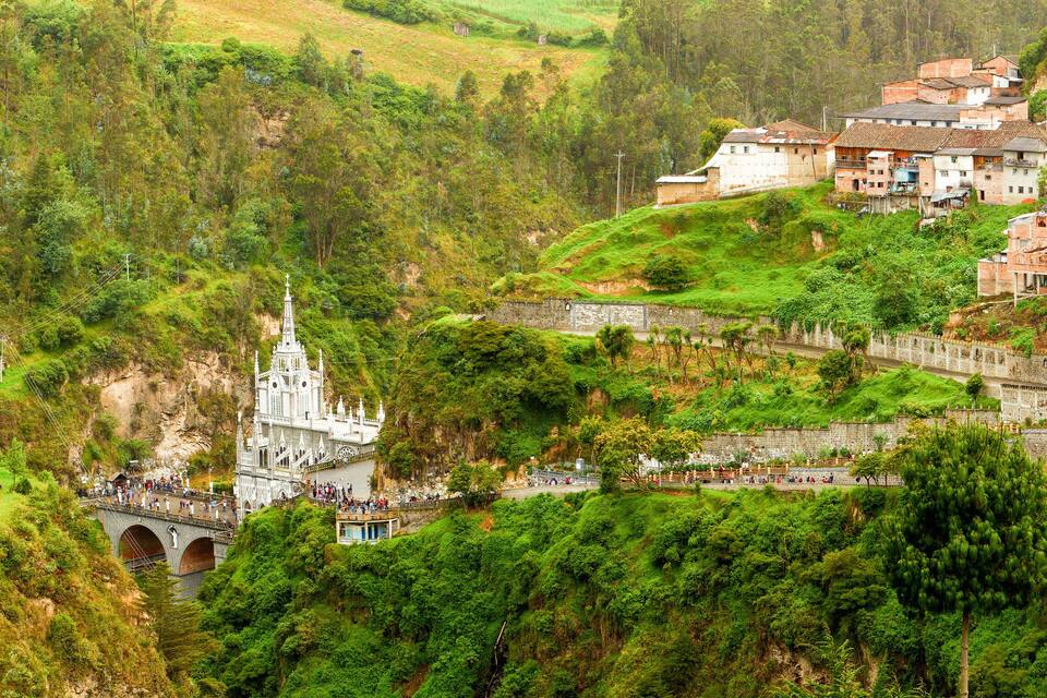 A lush green hillside with a white church and a stone bridge.