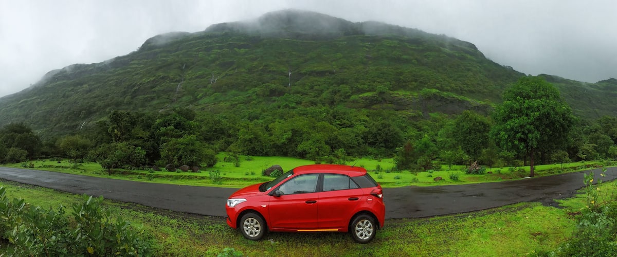 Red car parked on the road beside a mountain on a rainy day