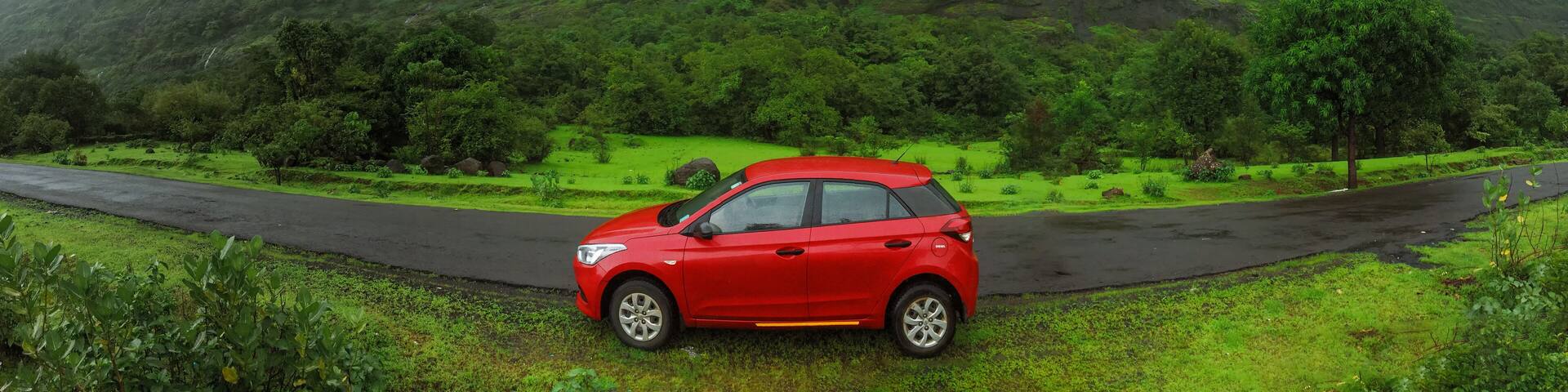 A red car parked on a wet road with a lush green mountain in the background.