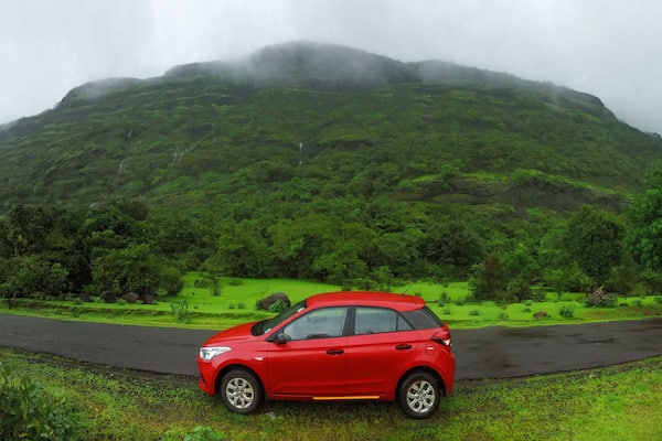 Red car parked on the road beside a mountain on a rainy day