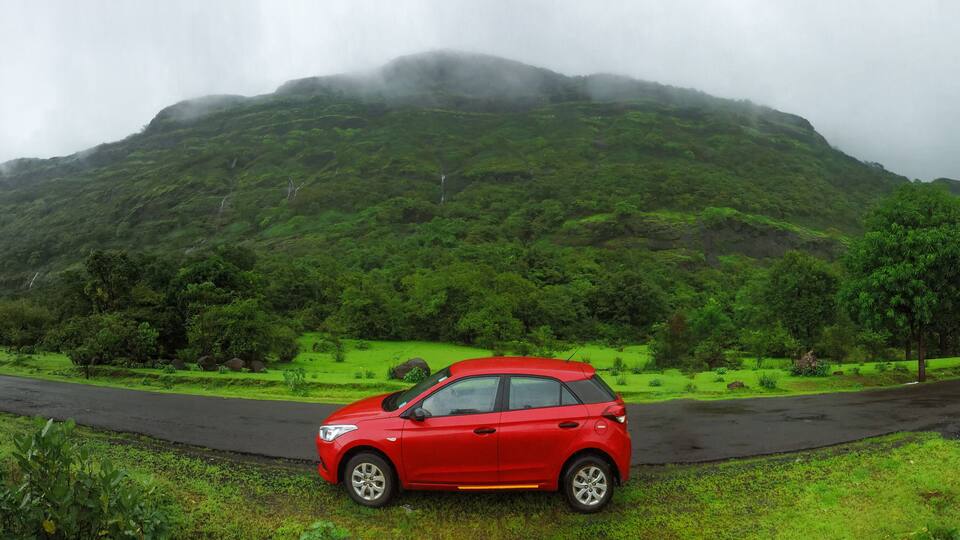 A red car parked on a wet road with a lush green mountain in the background.