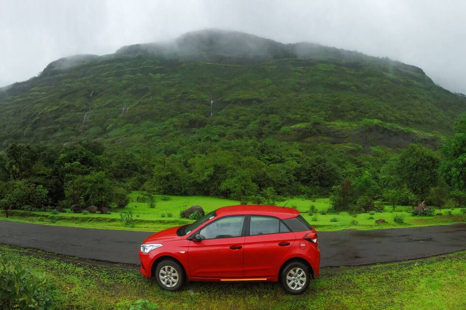 A red car parked on a wet road with a lush green mountain in the background.