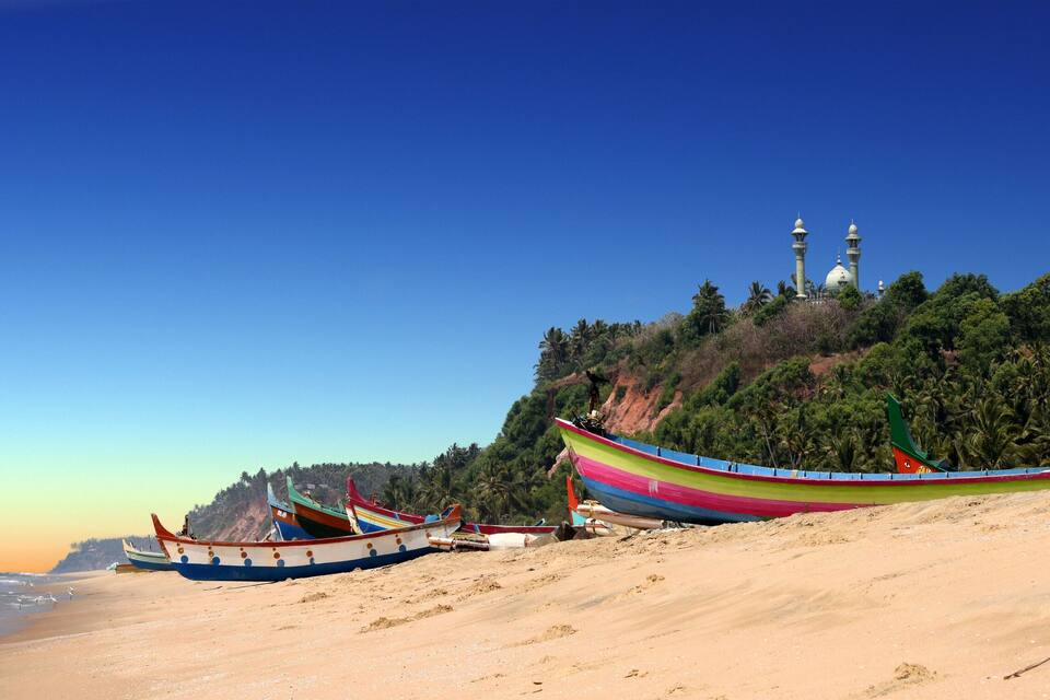 A beach with colorful boats and a mosque on a hill.