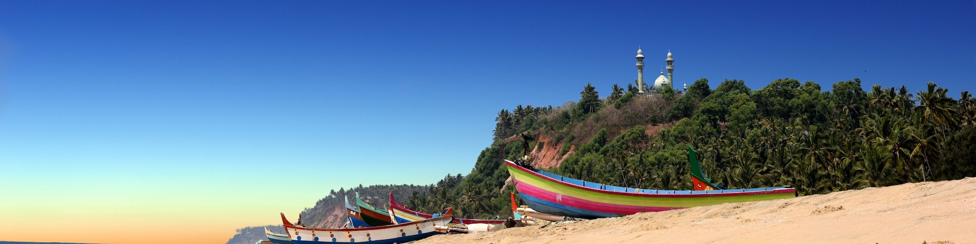 panoramic view of colorful fishermen boats in front of Varkala South Cliff with mosque on top, Kerala, India