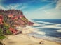 A coastal beach with a rocky cliff, palm trees, and a clear sky.