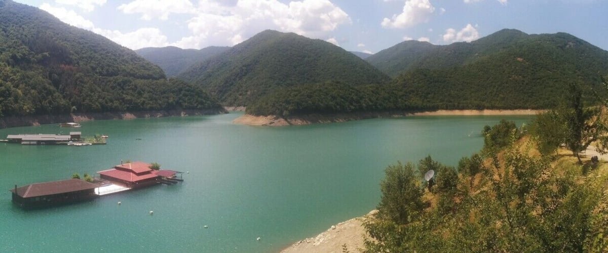 A river with boats, surrounded by forested hills.