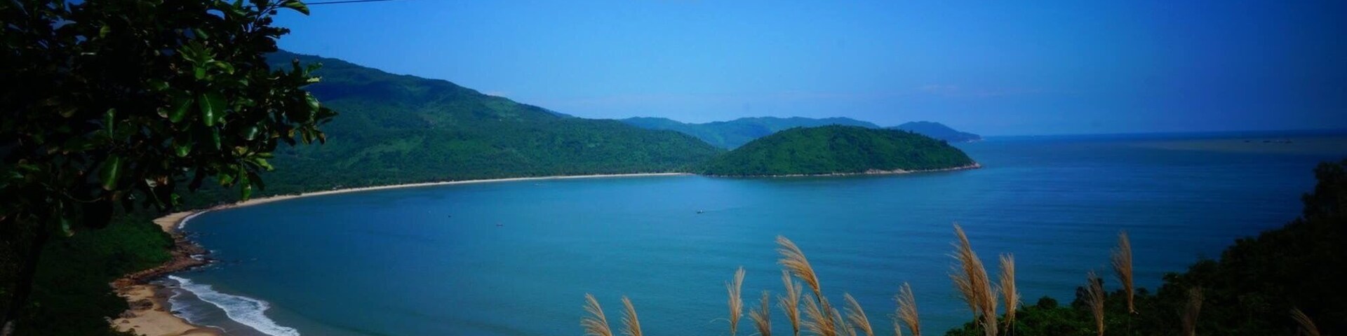 Un paisaje costero con playa arenosa, mar tranquilo y colinas verdes exuberantes.