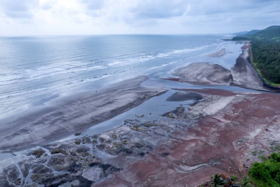 A coastal landscape with a sandy beach, rocky outcrops, and a forested hillside.