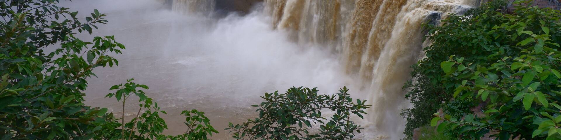 A large waterfall with multiple tiers of cascading water, surrounded by lush greenery and a cloudy sky.