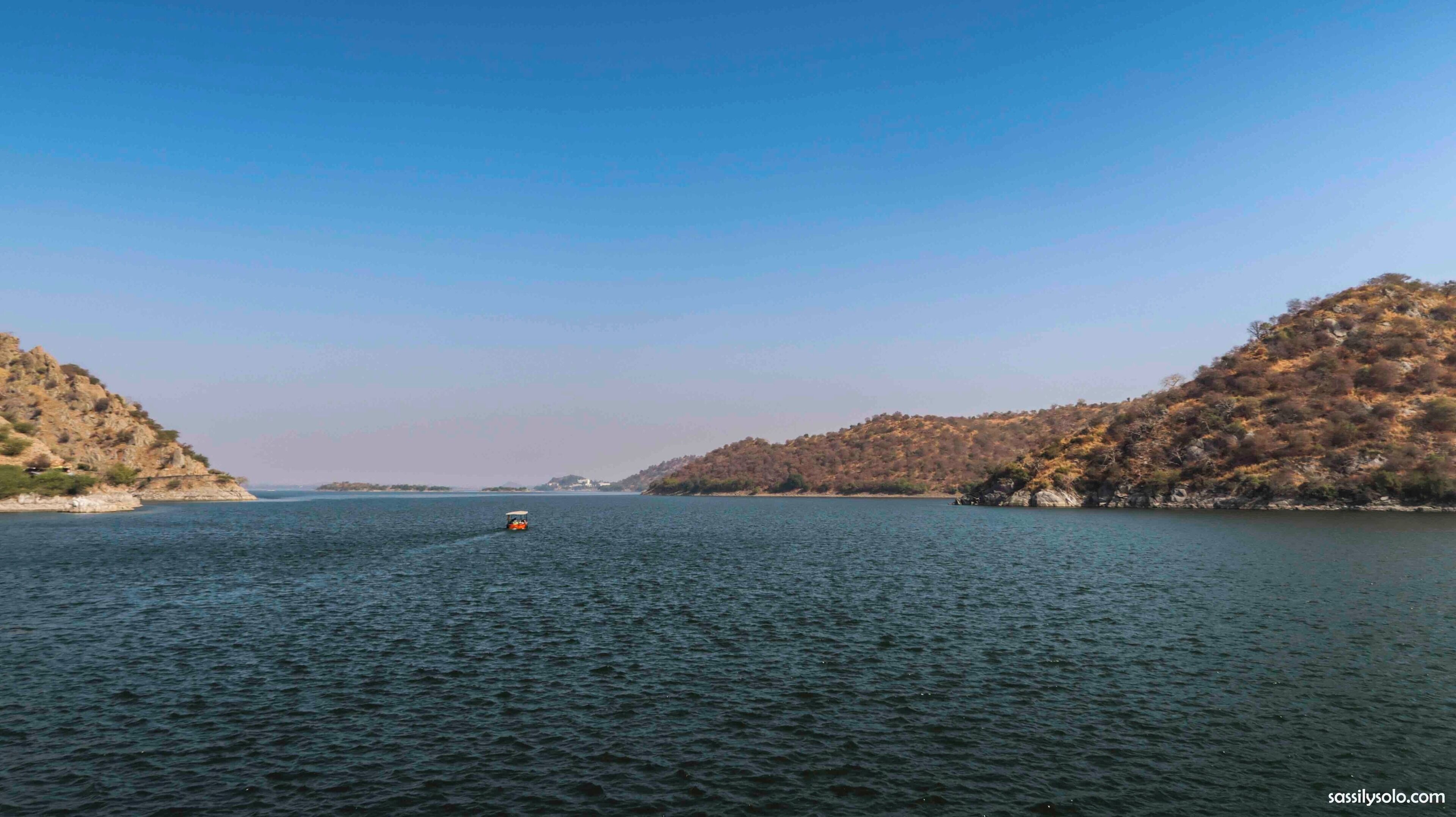 A calm lake with a boat in the center, surrounded by hills with sparse vegetation.