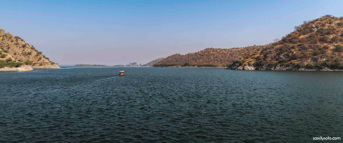 A calm lake with a boat in the center, surrounded by hills with sparse vegetation.