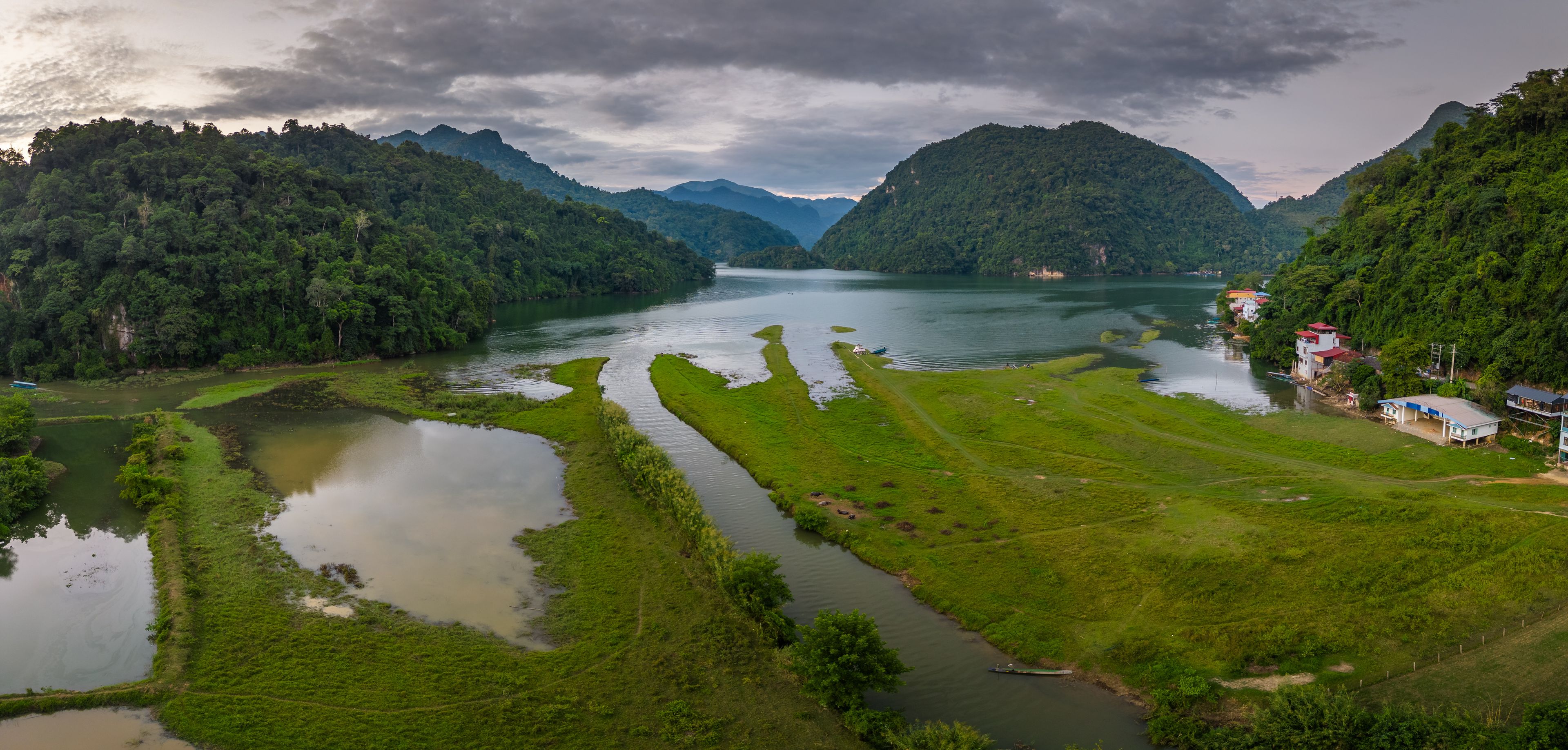 Un río serpentea por un valle exuberante con campos en terrazas y montañas boscosas al fondo, bajo un cielo nublado.