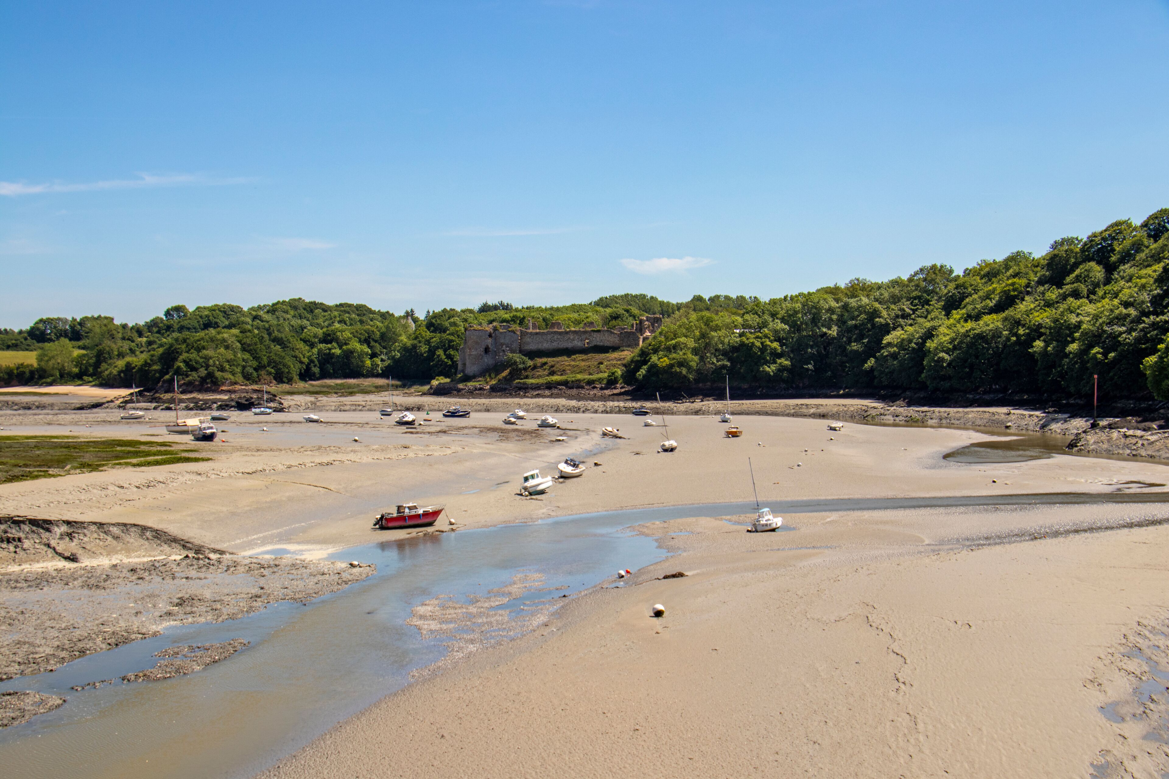 A coastal landscape with a sandy beach, a small river, and a historic stone structure in the background.