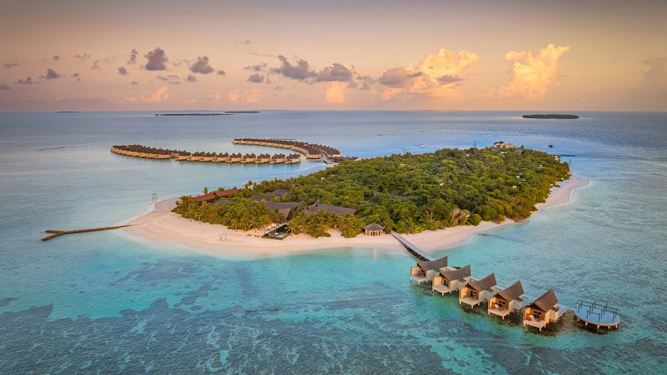 An aerial view of a tropical island with overwater bungalows, clear turquoise waters, and a small sandy beach.