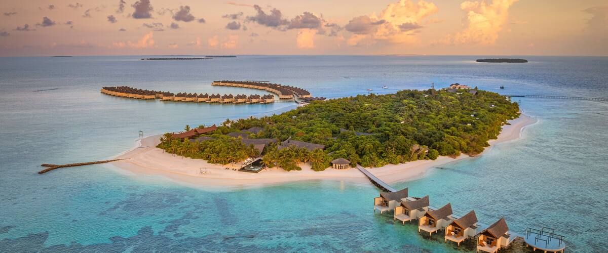 An aerial view of a tropical island with overwater bungalows, clear turquoise waters, and a small sandy beach.