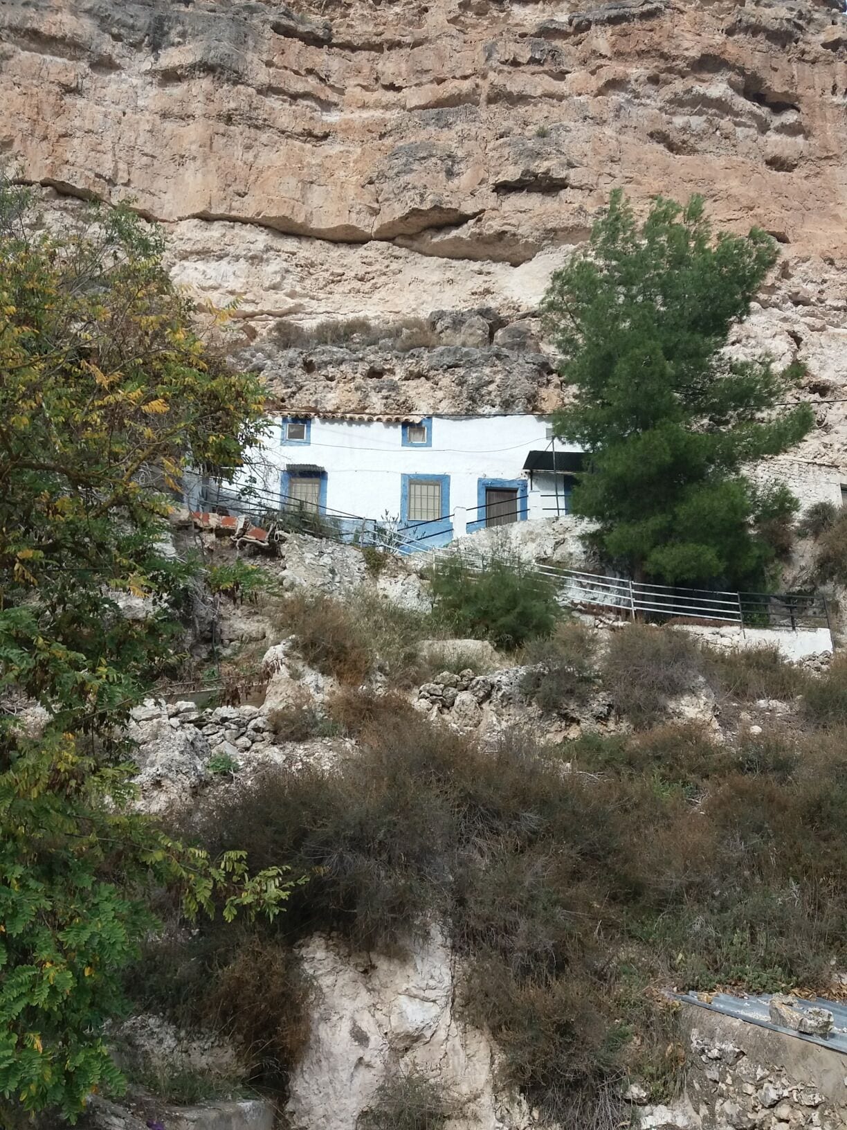A white building with blue trim nestled against a rocky cliff.