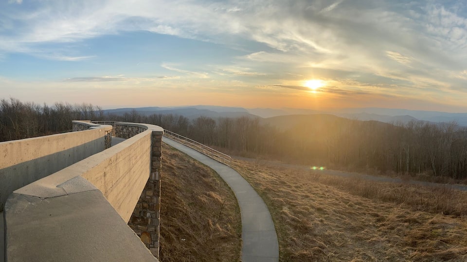 A concrete viewing platform overlooking a valley with a sunset in the background.