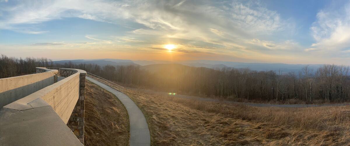 A concrete viewing platform overlooking a valley with a sunset in the background.