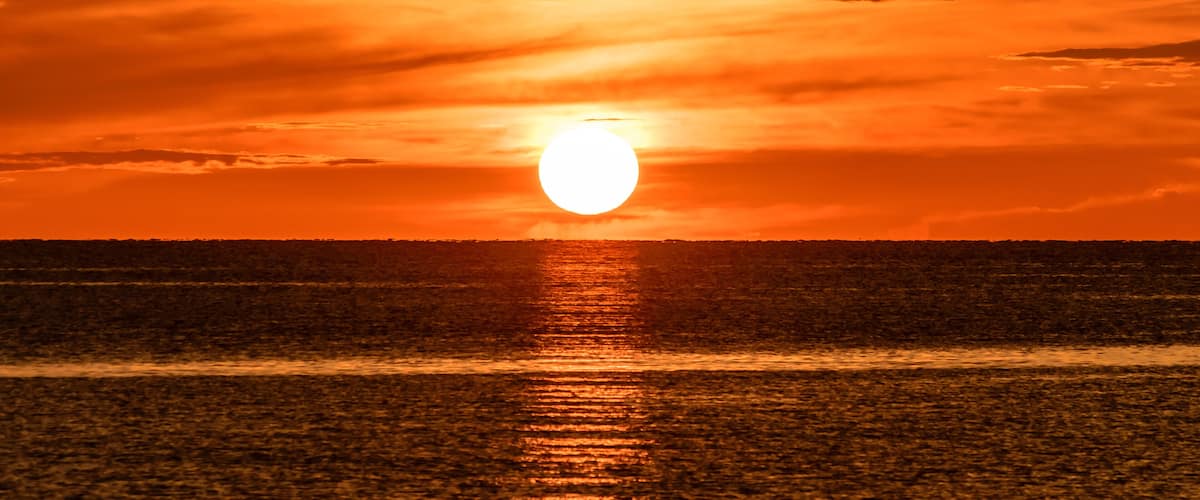 A sunset over a calm sea with a visible horizon line.