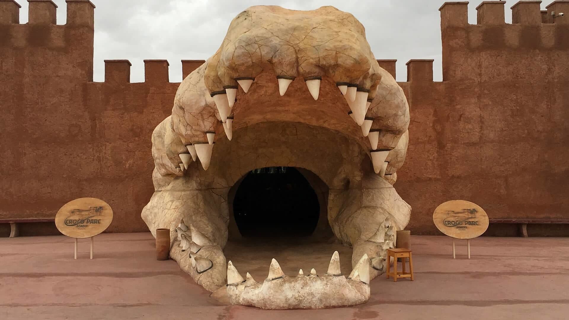 Una gran escultura realista de boca de dinosaurio con dientes, sobre un fondo que recuerda a un castillo.