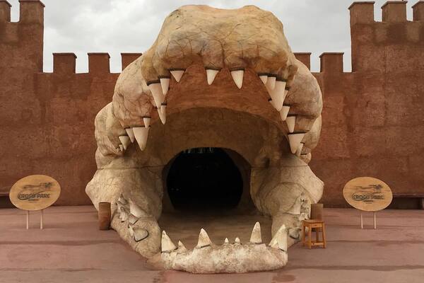 Une grande sculpture réaliste représentant la gueule d’un dinosaure, avec ses dents, placée sur un fond évoquant un château.