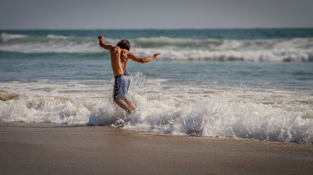 An unidentifiable skimboarder riding a small shorebreak wave on a beach. The image was made in Rosarito Mexico