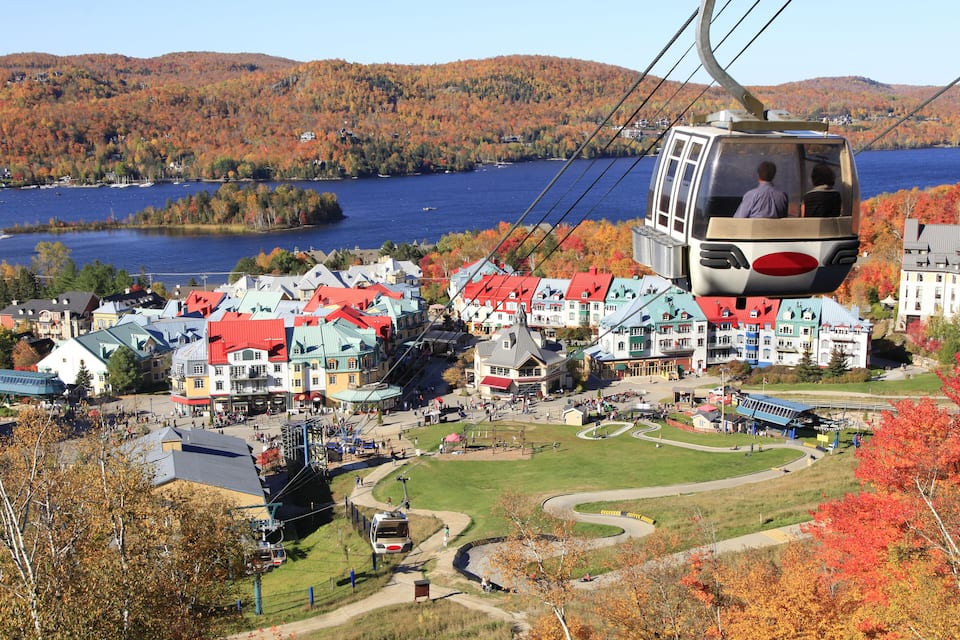 A cable car over a town with red-roofed buildings and a lake in the background.