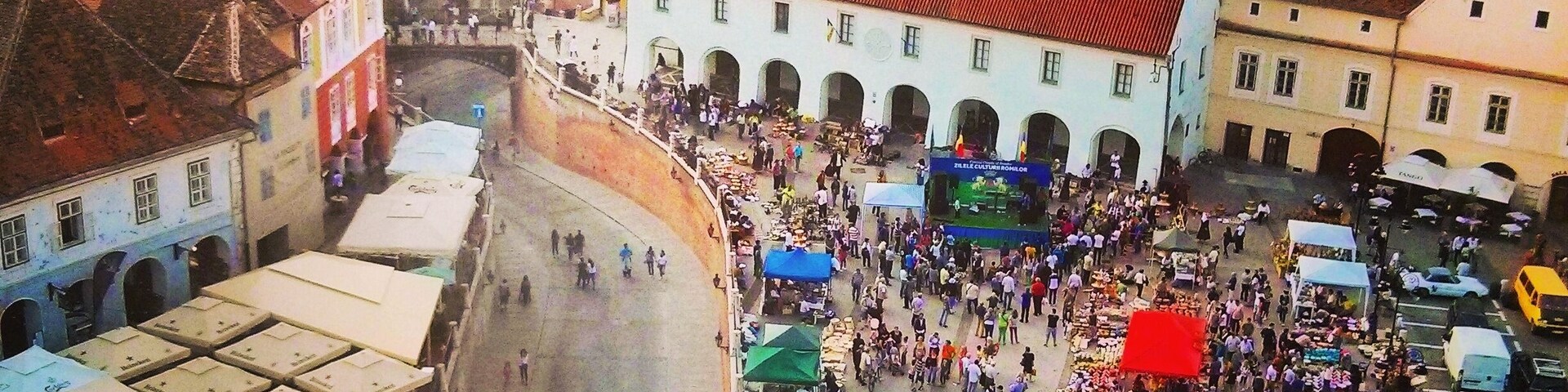 Vista aérea de uma praça de mercado movimentada, rodeada por edifícios históricos com telhados de terracota.