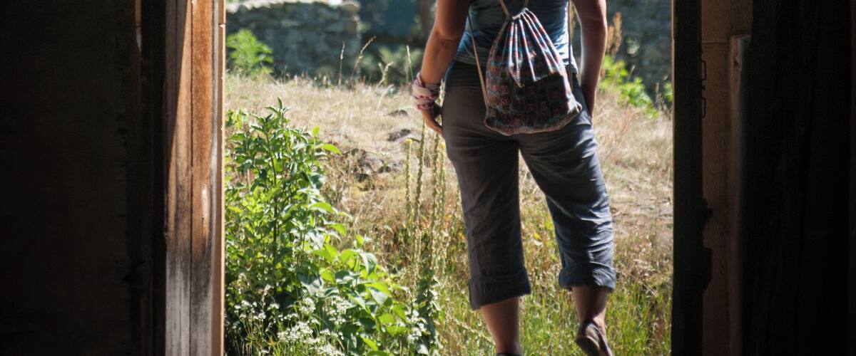 A person walking through an arched doorway into a natural landscape with trees and grass.