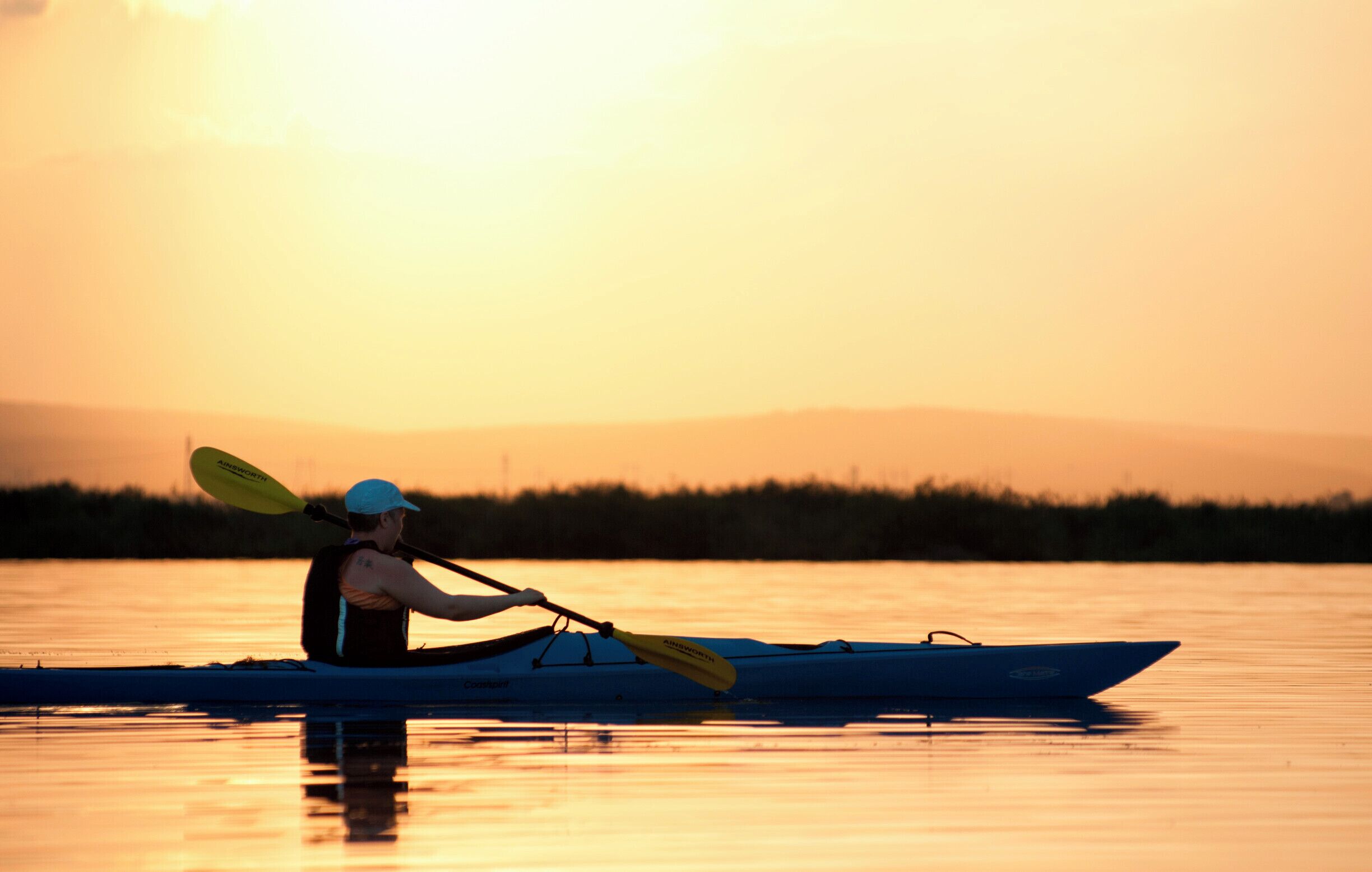 A person kayaking on a calm body of water during sunset.