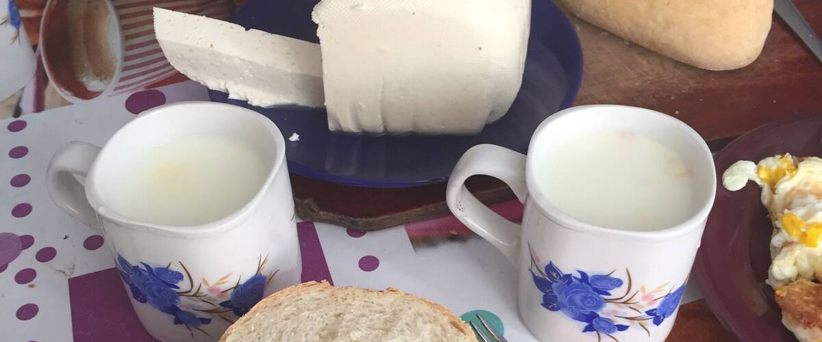 A meal with bread, eggs, tomatoes, and a cheese wheel on a table.
