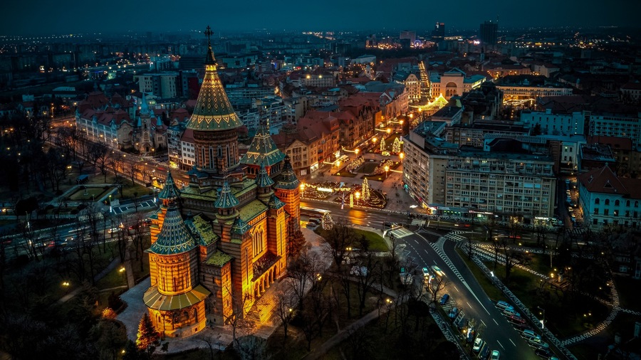 Un paisaje urbano nocturno con edificios iluminados y una iglesia destacada con cúpula.