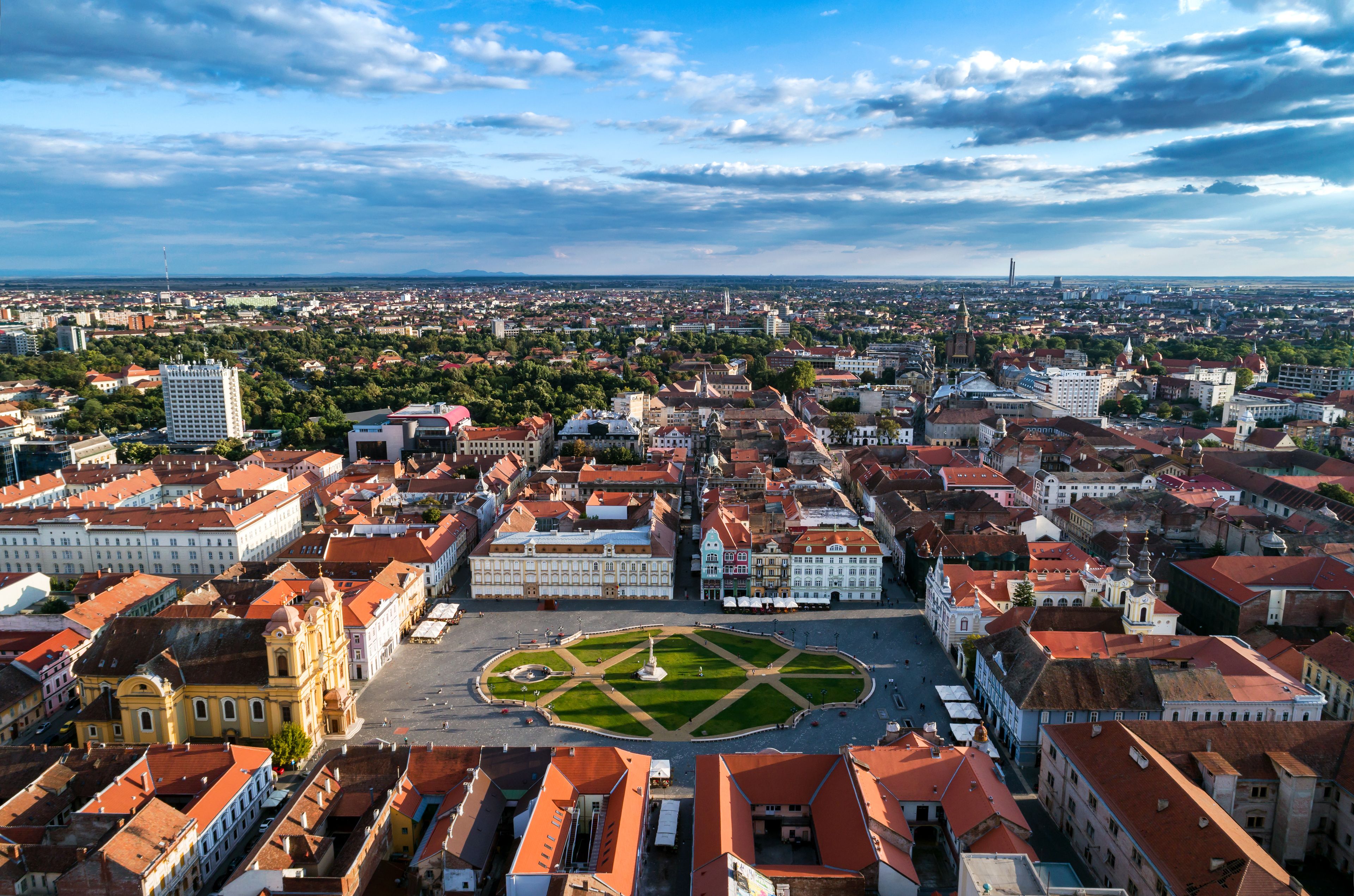A cityscape with historic buildings, a central square, and a distant view of a city skyline.
