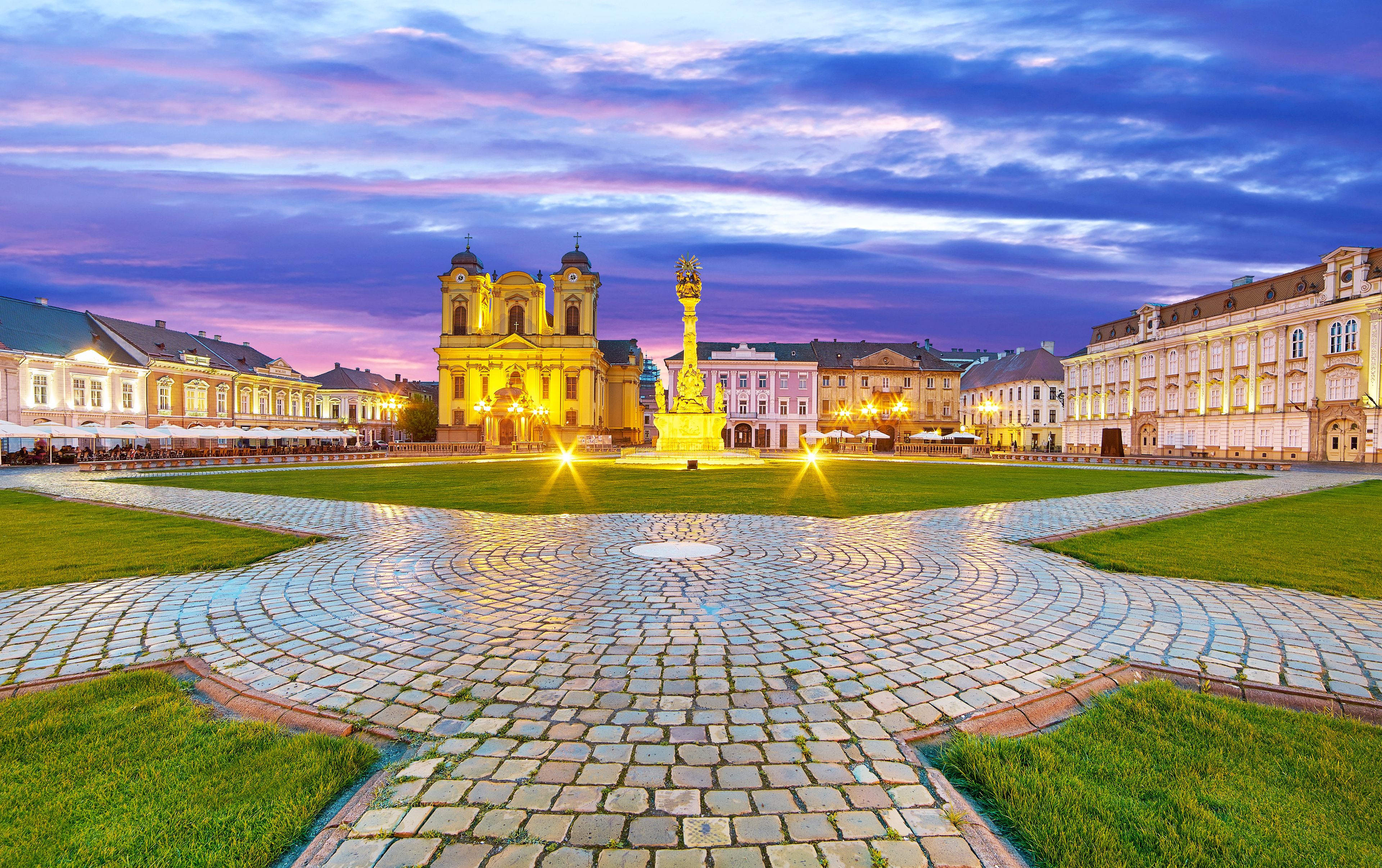 A historic square with a central fountain, surrounded by classical architecture and a cobblestone pavement.