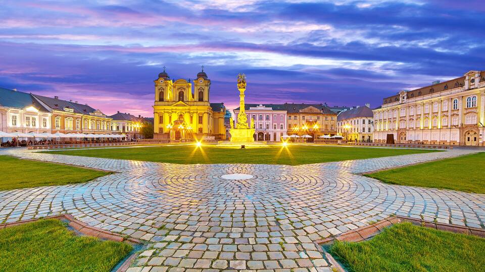 A historic square with a central fountain, surrounded by classical architecture and a cobblestone pavement.